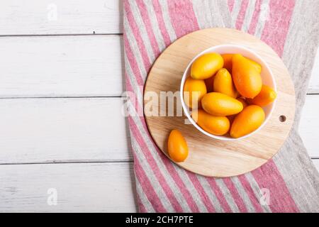 kumquats in un piatto bianco su sfondo di legno bianco, vista dall'alto, piatto, spazio per la copia. Foto Stock