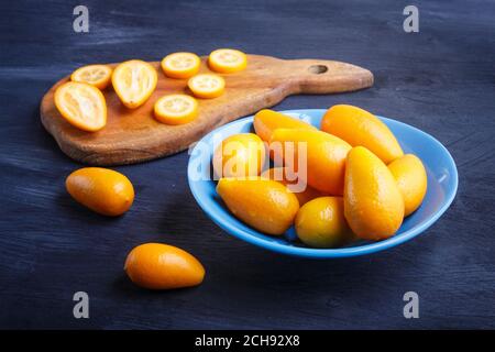 kumquats in un piatto blu su sfondo nero di legno, primo piano. Foto Stock