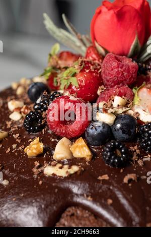 Primo piano di torta al cioccolato ripiena di panna, ricoperta di frutti di bosco e una rosa. Foto Stock