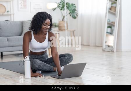 Allegra donna africana che si esercita a casa, utilizzando il computer portatile Foto Stock