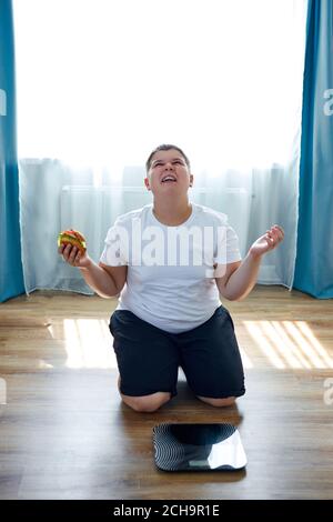 un bambino in sovrappeso è seduto sulle ginocchia vicino alle scale e urla, pensa che wnen si fermerà cibo spazzatura Foto Stock