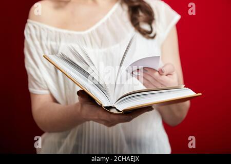 Il libro è in mani femminili. La ragazza gira pagine bianche su sfondo rosso Foto Stock