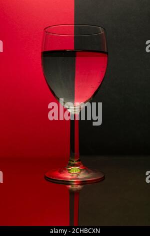 Un bicchiere di vino che riflette uno sfondo rosso e nero. Foto Stock