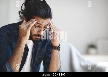 Giovane ragazzo indiano freelance che soffre di mal di testa dopo un duro lavoro giorno Foto Stock