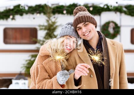 Sorridente coppia romantica in cappelli a maglia in posa con sparklers a. Campeggio invernale Foto Stock