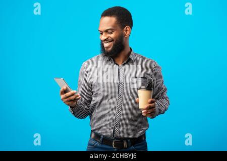 Sorridente uomo nero che testava al telefono bevendo caffè Foto Stock