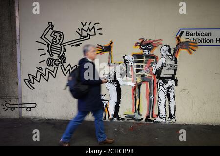 A man walks past one of two new murals painted by the artist Banksy near the Barbican Centre in London. The works mark the opening of an exhibition by American artist Jean-Michel Basquiat at the arts venue. Stock Photo