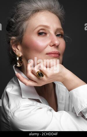 Ritratto di una bella donna anziana in una camicia bianca con trucco classico e capelli grigi. Foto Stock