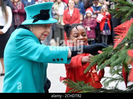 La regina Elisabetta II e Shylah Gordon, di 8 anni, attaccano un babble ad un albero di Natale durante la sua visita a Coram, la più antica associazione di beneficenza per bambini del Regno Unito, per aprire il Queen Elizabeth II Center alla sua base nel centro di Londra. Foto Stock