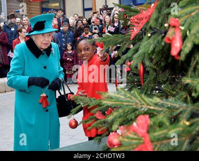 RITRASMETTENDO IL NOME DI MODIFICA DA SHYLAH GORDON A SHYLAH GORDON-CLARKE LA DIDASCALIA CORRETTA SOTTO la regina Elisabetta II e Shylah Gordon-Clarke, di 8 anni, attaccano un bauble ad un albero di Natale durante la sua visita a Coram, la più antica carità per bambini del Regno Unito, per aprire il Queen Elizabeth II Center alla sua base nel centro di Londra. Foto Stock