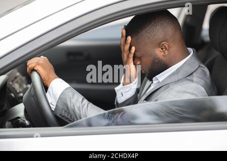 Uomo d'affari africano sconvolto che sfrega la testa mentre guida l'auto Foto Stock