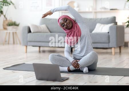 Home Training. Donna musulmana nera in hijab praticare sport online con il laptop