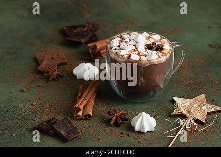 Coppa di cioccolato caldo o cacao con marshmallows e stella di anice, pezzi di cioccolato, meringa e spezie su sfondo verde. Inverno tradizionale Foto Stock