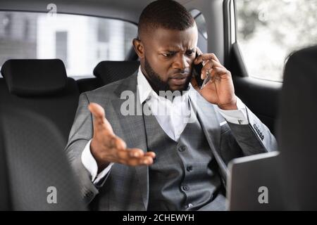 Arrabbiato uomo d'affari afroamericano che parla al telefono in auto Foto Stock