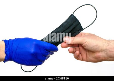 mano in un guanto medico protettivo blu mani su una maschera medica nera a una mano non protetta sul fondo bianco Foto Stock