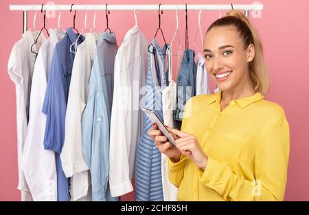 Donna felice che tiene il telefono in piedi vicino al rack con vestiti Foto Stock