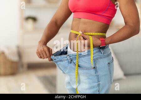 Donna dopo perdita di peso che misura la vita indossando jeans oversize all'interno, tagliato Foto Stock