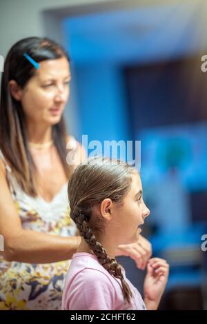 Donna che combatte i capelli della figlia a casa prima di andare a scuola. Foto Stock