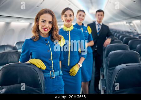 Felice squadra di aviazione allegra in elegante blu e blu scuro uniforme in piedi nel salone dell'aereo Foto Stock
