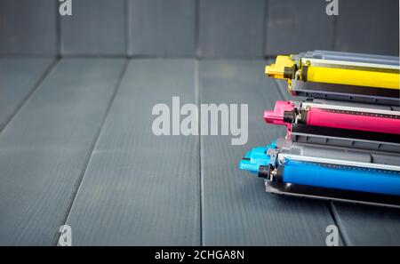 Tre cartucce di toner usate in una stampante laser a colori impilate su sfondo grigio in legno per il riciclaggio Foto Stock
