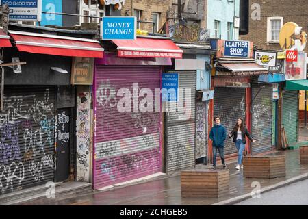 La gente passa accanto a negozi chiusi su Camden High Street, nel nord di Londra, mentre il Regno Unito continua a bloccarsi per contribuire a frenare la diffusione del coronavirus. Foto Stock