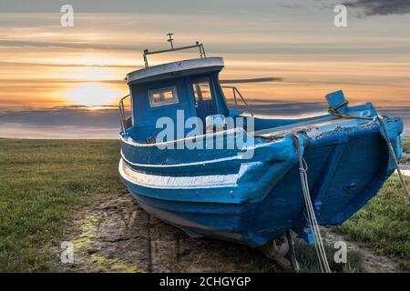 vecchia barca da pesca illuminata dal tramonto a bassa marea in estuario Foto Stock