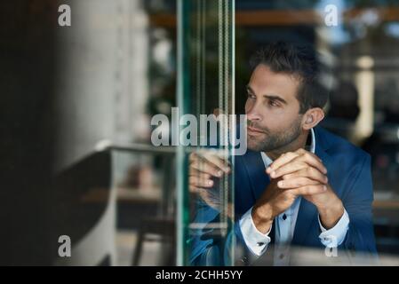 Giovane uomo d'affari seduto accanto a una finestra all'interno di un caffè Foto Stock