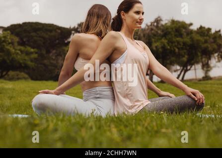 Due donne in forma fisica sedute in un parco con le loro spalle rivolte l'una verso l'altra e facendo allenamento. Donne che fanno esercizi di fitness seduti in un parco. Foto Stock