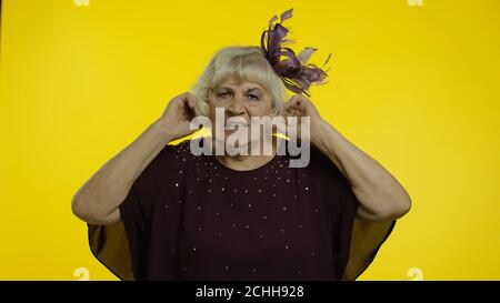 Non vuoi ascoltare. Irritato anziana anziana donna irritata che copre le orecchie e gesturing No, evitando consigli, ignorando il rumore sgradevole. Anziana elegante nonna donna su sfondo giallo Foto Stock