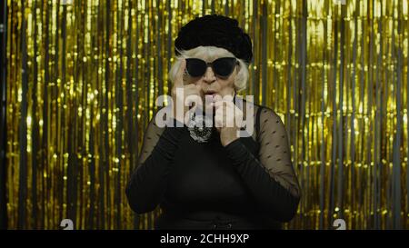Affascinante anziana anziana con triste espressione meditativa, fantasia, che ricorda piacevoli ricordi, facendo un'idea positiva. Pensieroso anziano elegante nonna donna su sfondo dorato Foto Stock