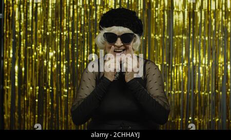 Affascinante anziana anziana con triste espressione meditativa, fantasia, che ricorda piacevoli ricordi, facendo un'idea positiva. Pensieroso anziano elegante nonna donna su sfondo dorato Foto Stock