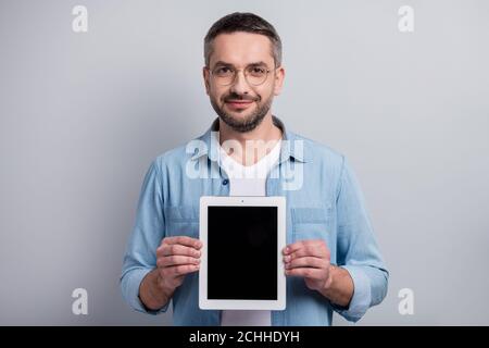 Primo piano ritratto del suo bello attraente allegro contenuto grigio-capelli guy venditore che tiene nelle mani nuovo tablet dimostrando isolato sopra grigio chiaro Foto Stock