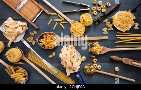 Concetto di cucina della pasta. Pasta cruda di varie forme e vintage attrezzature culinarie piatto adagiato su sfondo blu tavola di legno, vista dall'alto Foto Stock