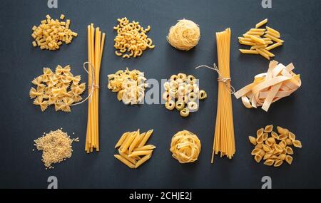 Concetto di cucina della pasta. Varietà di forme di pasta cruda piatte su sfondo nero, vista dall'alto Foto Stock