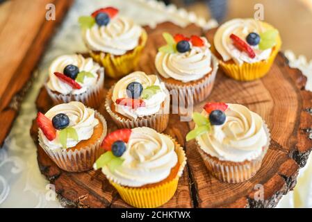 Cupcake per Buon San Valentino. Su vassoio marrone di legno crema dolce con fragole e mirtilli Foto Stock