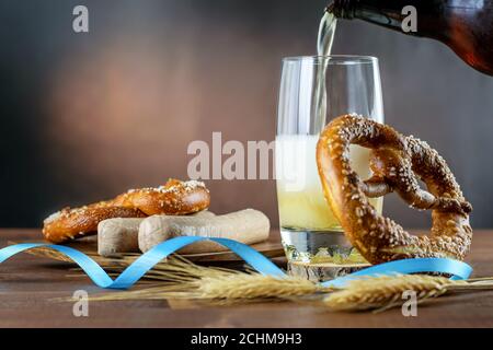 Birra bavarese leggera che si versa in vetro, salsicce bianche bollite e pretzel sul legno nel giorno dell'Ottobre. Foto Stock