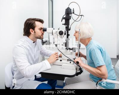 Optometristo che fa il controllo della vista per una donna anziana alla clinica moderna. Esame visivo e diagnostica visiva Foto Stock