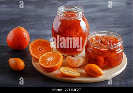 Marmellata di mandarino e kumquat in un vaso di vetro con frutta fresca su un tavolo di legno nero. Fatti in casa, spazio per le copie, primo piano. Foto Stock