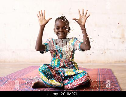 African Fun Party Girl, donna sorridente che lancia i confetti, contro uno sfondo bianco con Copy Space Foto Stock