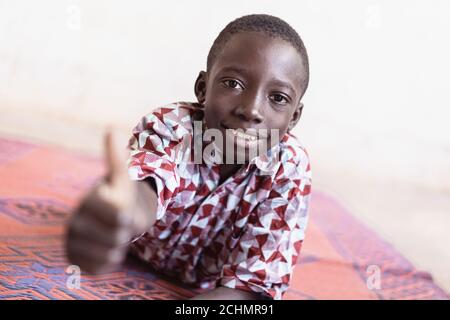 Scolaro africano che dà i pollici di fronte a White Sfondo Foto Stock