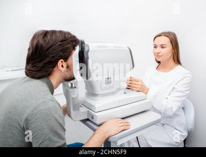 Donna optica che controlla la vista al paziente di sesso maschile in una clinica utilizzo di apparecchiature oftalmiche diagnostiche Foto Stock