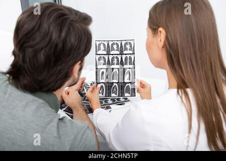 Pulmonologa che mostra ad un paziente di uomo una scansione CT dei suoi polmoni durante una consultazione. Polmonite, coronavirus, malattie polmonari Foto Stock
