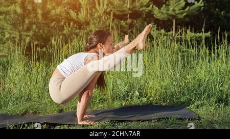 Donna esegue yoga asana all'aperto in giornata di sole, luce del sole Foto Stock