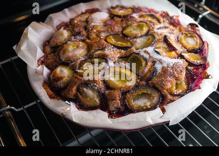 Torta di prugne rustica appena sfornata a casa nel forno in cucina. Cottura fatta in casa. Piatto da forno vegano. Foto Stock