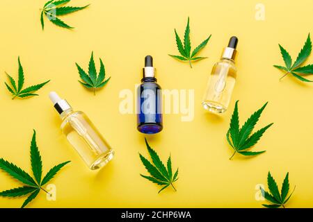 Siero di olio di canapa in contagocce di vetro con foglia di cannabis. Foglie di cannabis con prodotti cosmetici su sfondo giallo Foto Stock