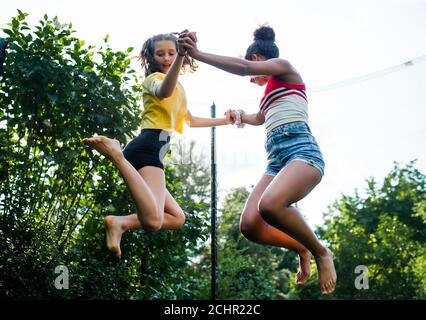 Vista ad angolo basso di giovani ragazze amici all'aperto in giardino, saltando su trampolino. Foto Stock