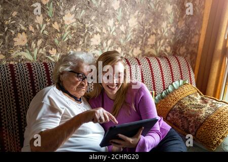 Donna anziana e nipote seduta su divano con tablet Foto Stock