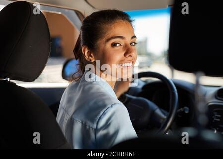 Ritratto di giovane donna sorridente che guida l'auto e guardando la macchina fotografica, girato dalla fila posteriore, spazio di copia Foto Stock