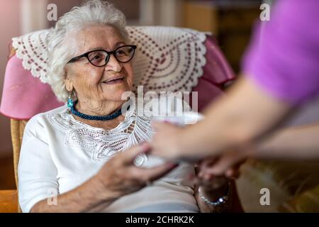 Un'infermiera domestica utile dà ad una femmina anziana una tazza di tè caldo Foto Stock
