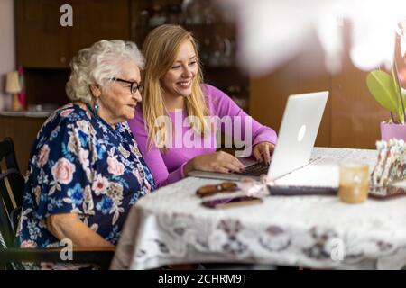 Nipote adulta che insegna alla nonna anziana di usare il computer portatile Foto Stock